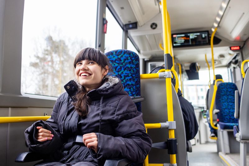 A happy teenage girl with neurodiversity (Rett Syndrome) sits in a wheelchair riding public transportation in Sweden. She is dressed in a warm winter coat, smiling and enjoying the ride. The image captures inclusion, accessibility, and independence in everyday life.