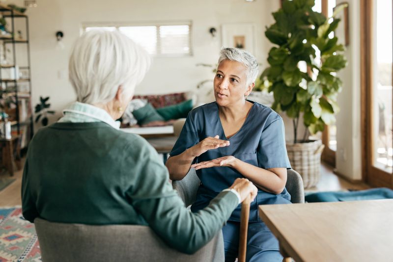 A healthcare worker assisting an elderly woman with online medical resources on a tablet.