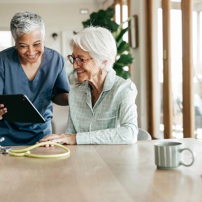 Caregiver and elderly woman share a joyful moment looking at a tablet.
