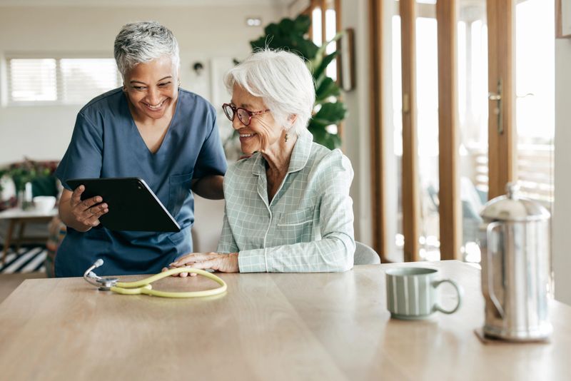 A healthcare worker assisting an elderly woman with online medical resources on a tablet.