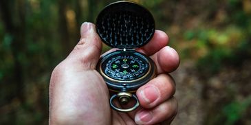 Hand holding an open compass in a forest.