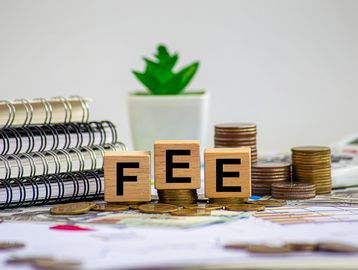 Wooden blocks spelling FEE on coins, surrounded by notebooks and a plant.
