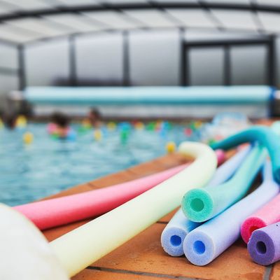 Zwemstokken bij een zwembadrand met mensen in het water.