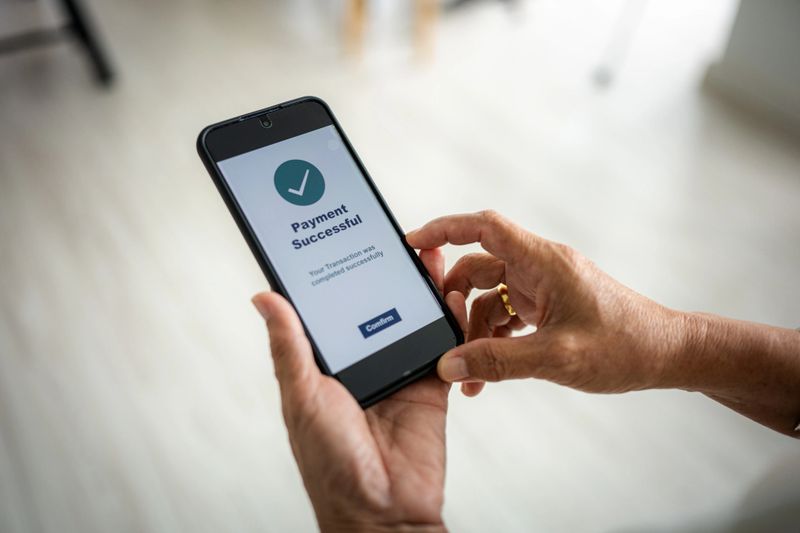 A senior woman is holding a smartphone displaying a payment successful message with a green check mark.