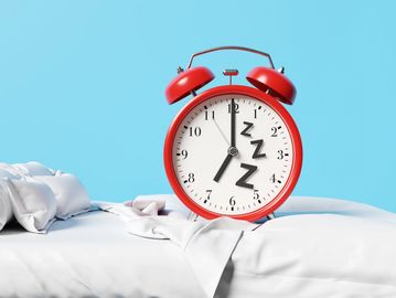 Red alarm clock with Zzz symbols on a bed with white sheets.