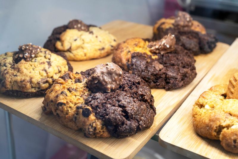 Freshly baked cookies with chocolate and hazelnut toppings are displayed on wooden boards, ready to be enjoyed