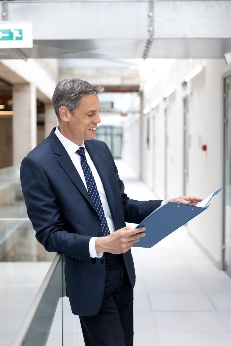 Mature / senior age male looking and holding his note pad with financial documents report at office