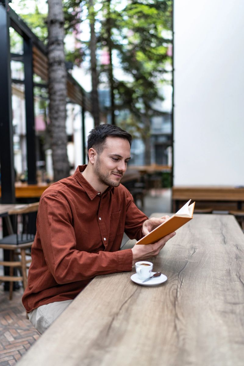 Young man enjoying a peaceful moment in an outdoor cafe, reading a book and drinking coffee