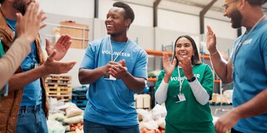 Volunteers happily clapping and celebrating in a warehouse filled with supplies.