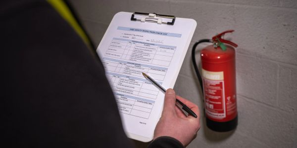Person inspecting a fire safety checklist near a fire extinguisher.