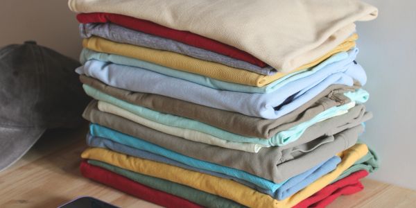 Neatly folded colorful clothes stacked on a wooden table.