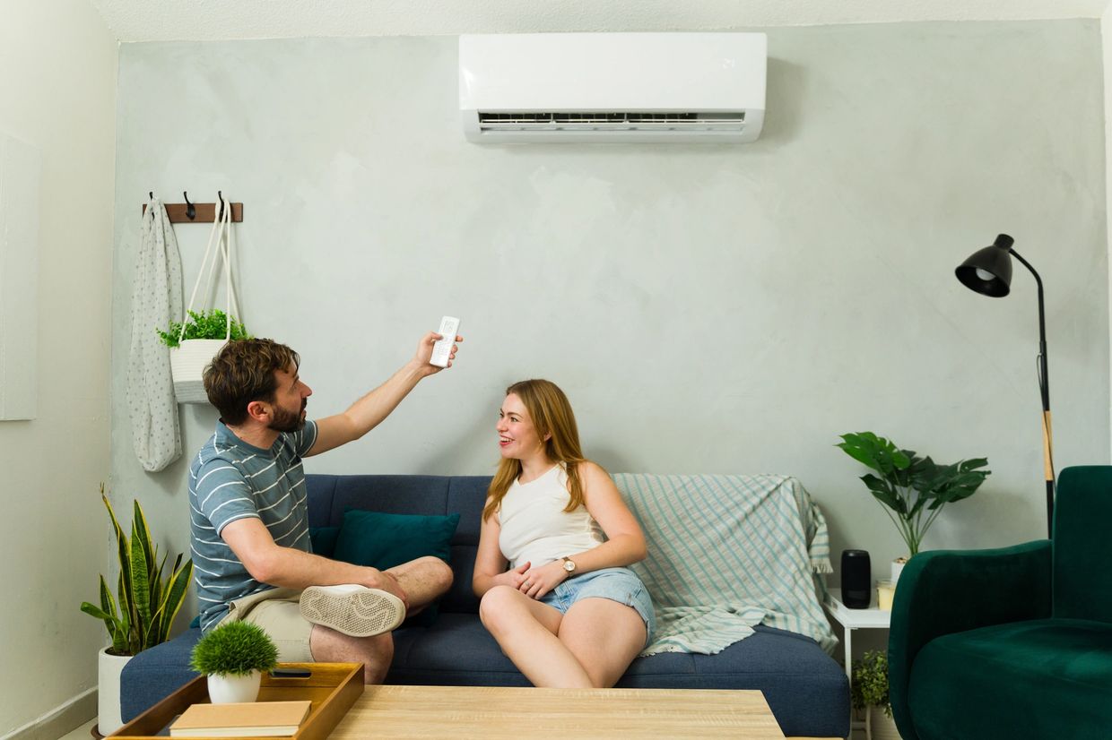 Couple relaxing on couch, man holding remote towards air conditioner.