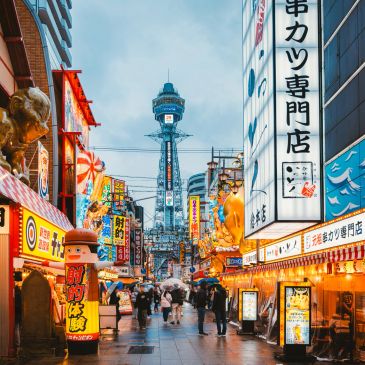 Busy street in Japan with Tsutenkaku Tower in the background.