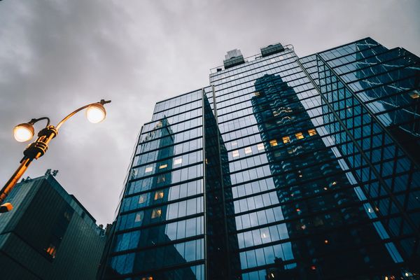 Modern glass skyscraper reflecting city buildings under cloudy sky.