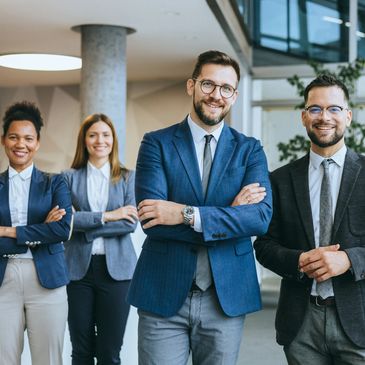 Vier Geschäftsleute lächeln selbstbewusst in einem modernen Büro.
