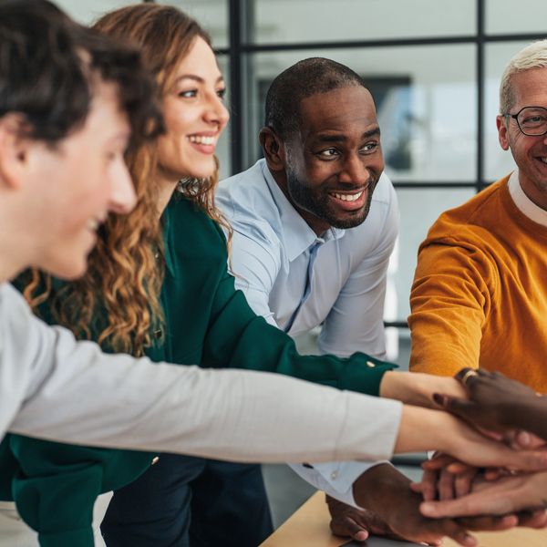 A diverse group of colleagues joining hands in teamwork and celebration.