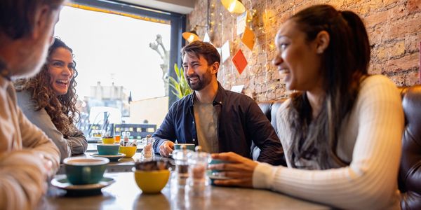 Four friends laughing and chatting in a cozy café with coffee cups on the table.