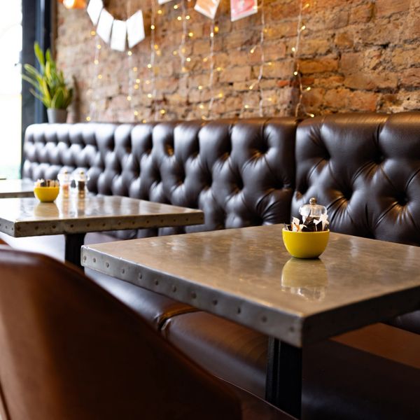 Cozy cafe seating with tufted leather bench and warm brick wall.