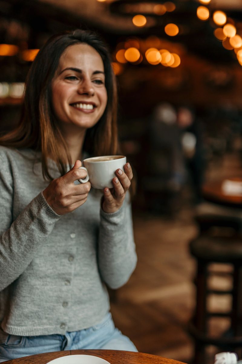 Young woman smiles while holding a warm cup of coffee, enjoying the cozy atmosphere of a cafe