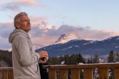 Older man in a hoodie enjoying a mountain view at sunset.