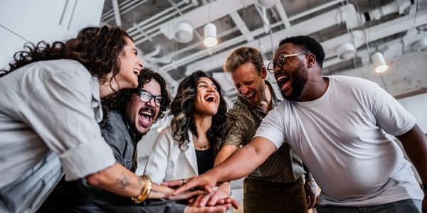 A diverse group of colleagues laughing and joining hands in a team huddle.