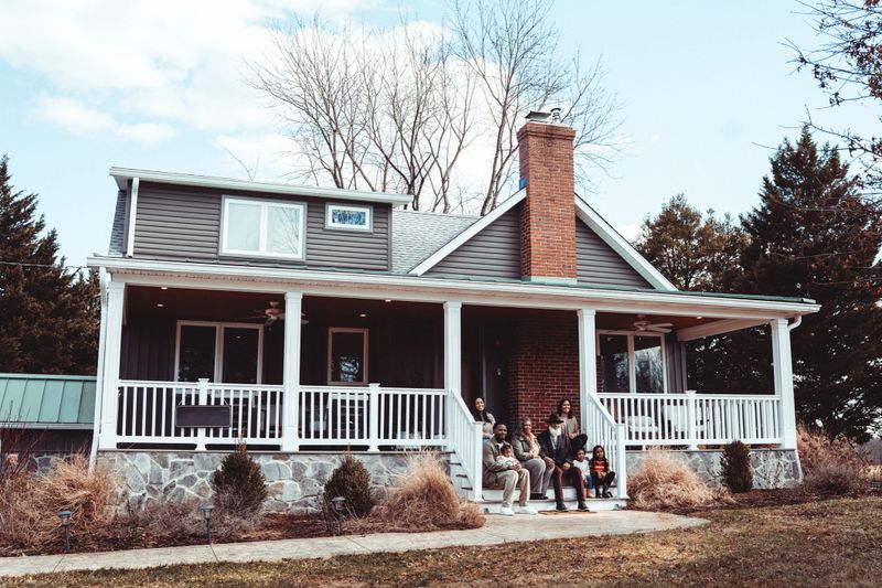Portrait of a loving multiracial multi-generation family smiling directly at the camera while gathered together on the front steps of a rural farmhouse during a weekend family reunion.