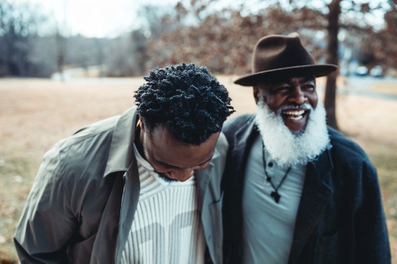 An active and healthy senior Black man laughs with his adult son while spending time together outside on a cool winter day.