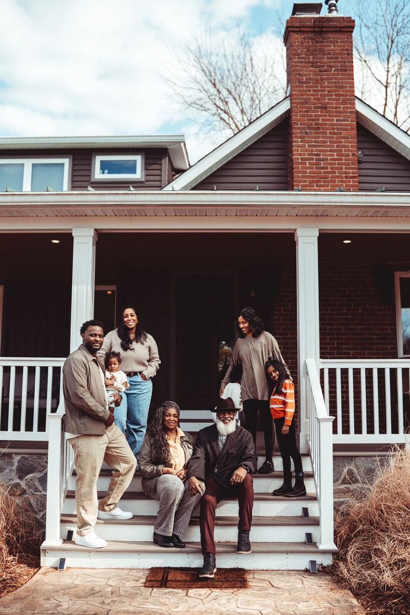 Portrait of a loving multiracial multi-generation family smiling directly at the camera while gathered together on the front steps of a rural farmhouse during a weekend family reunion.