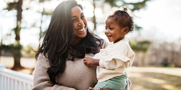 Happy woman holding a smiling baby outdoors.
