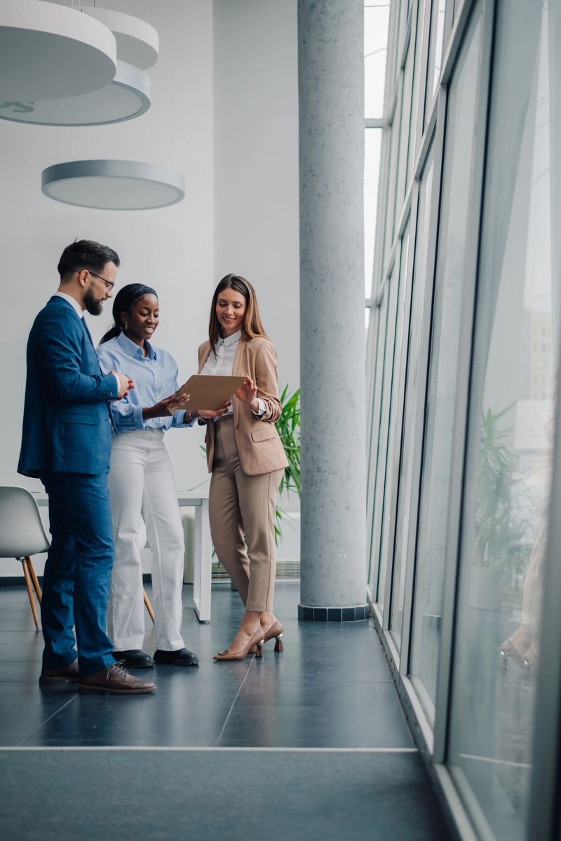 Three business colleagues are standing in a modern office, collaborating and discussing work-related matters using a digital tablet
