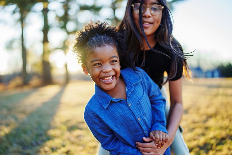 An adorable preschool age multiracial girl of African American and Indian descent laughs while playing with her older cousin outside on a sunny day while on family vacation together.