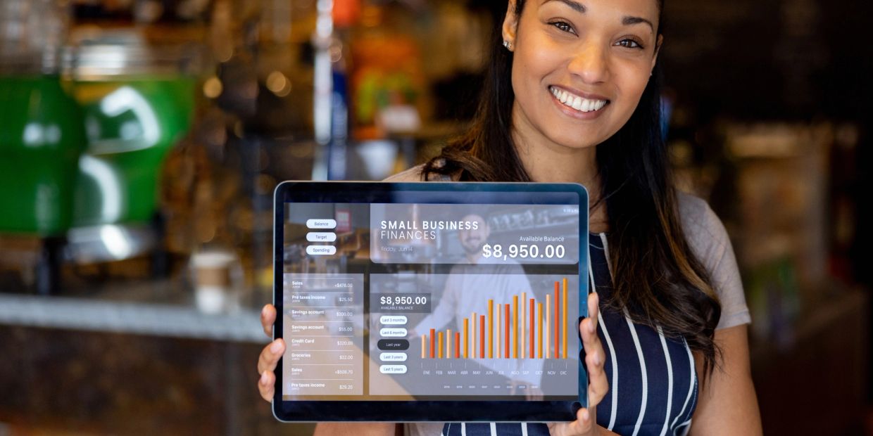 Smiling woman holding tablet showing small business finances and balance.