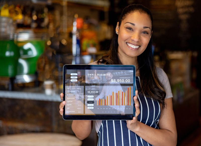 Portrait of a happy cafe owner showing the growth in her business finances using a tablet and looking at the camera smiling