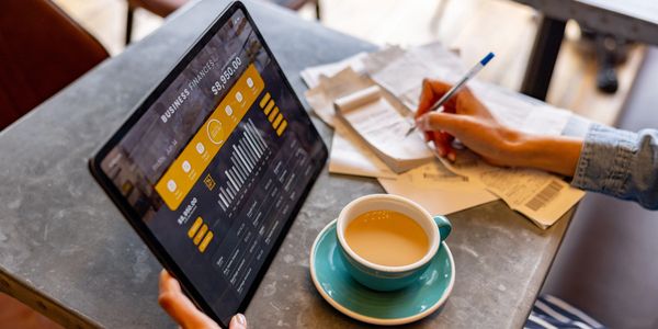 Person analyzing business finance data on a tablet while taking notes with coffee nearby.