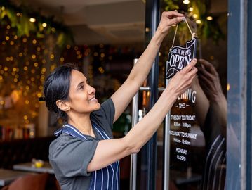 Woman opening a store by putting up an open sign.