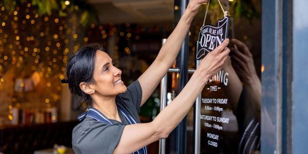 A woman hangs an open sign on a restaurant door.