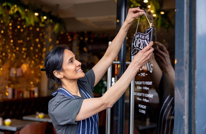 Happy female business owner hanging an open sign on the door at a cafe - small business concepts