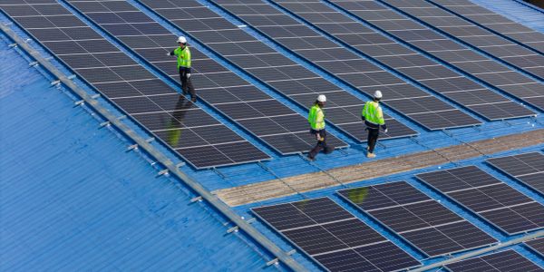 Workers inspecting solar panels on a blue rooftop.