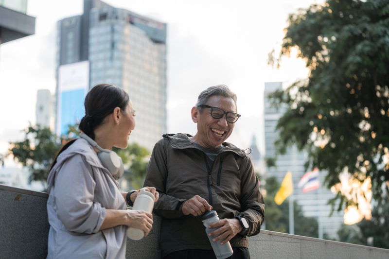 Senior couple taking a break from their run, chatting and laughing at a funny video in their smartphone. Their laughter fills the air, genuine and lighthearted, their faces bright with joy