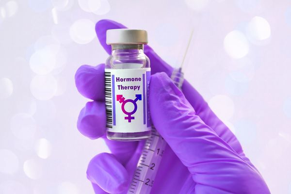 Gloved hand holding hormone therapy vial and syringe.