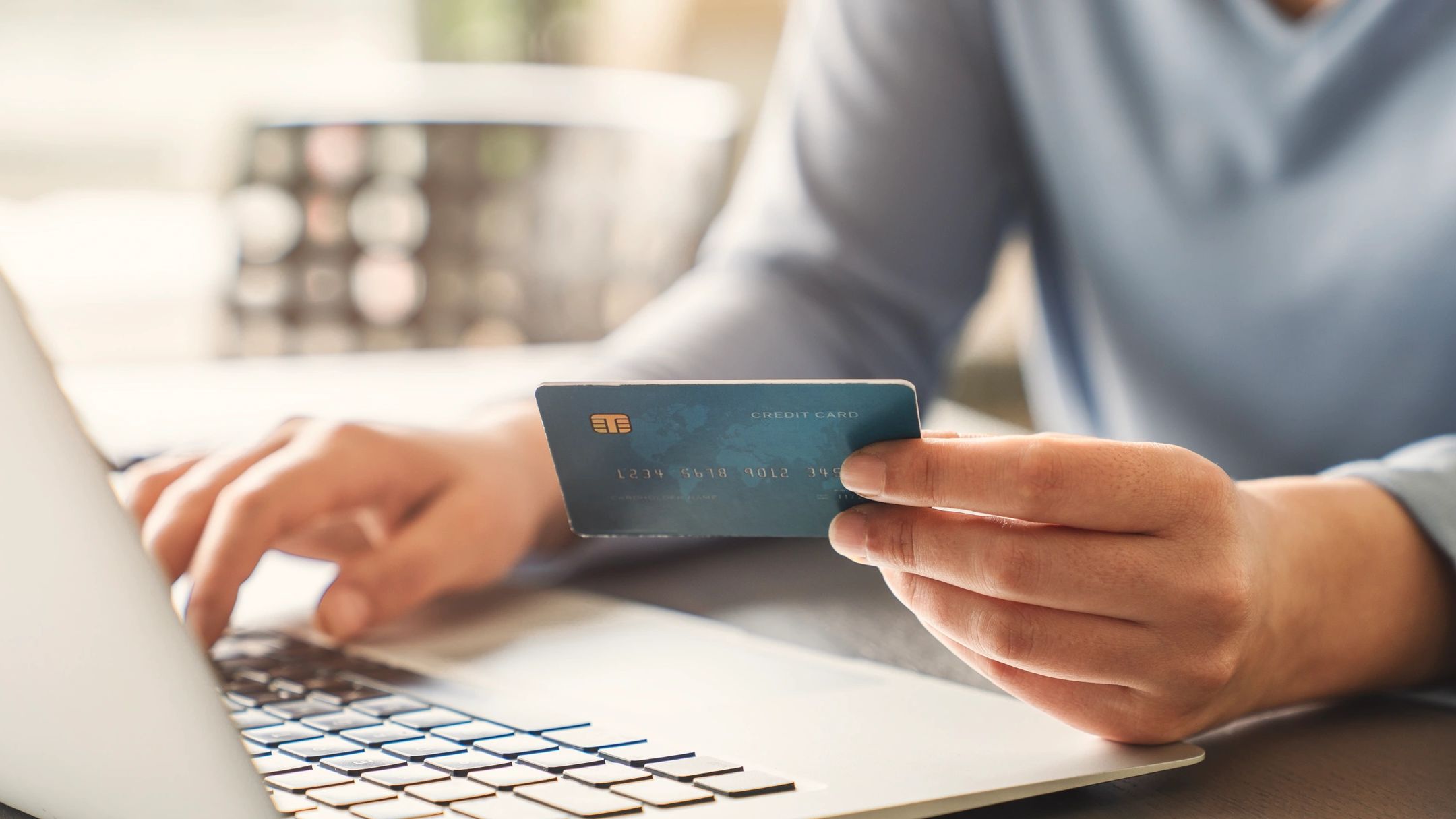 Person holding credit card while using laptop.