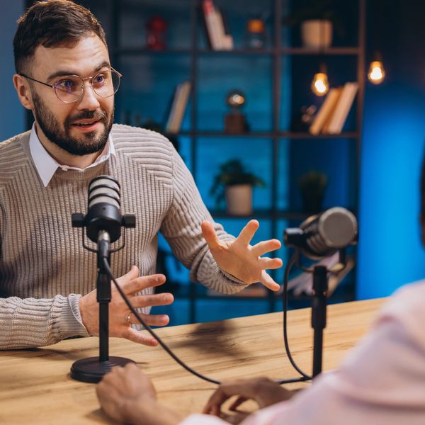 Man in glasses explains passionately during a podcast recording.