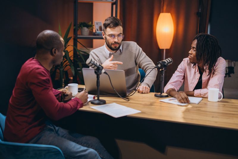 Content creator speaking into condenser microphone while working on laptop in contemporary recording studio environment