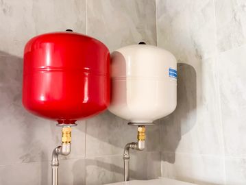 Two expansion tanks, one red and one white, mounted on a tiled wall.