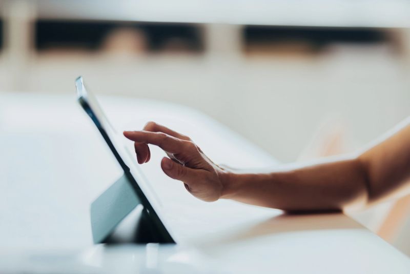 A close-up image of a hand interacting with a tablet placed on a table in bright lighting, symbolizing modern technology, connection, and digital lifestyles.