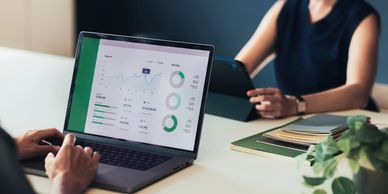 Two people reviewing financial charts and data on a laptop and tablet.
