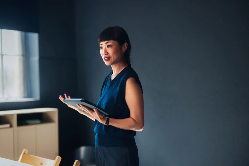 Professional woman using a tablet while delivering a presentation in a stylish office space. Emitting confidence, showcasing leadership qualities, and highlighting modern technology in a corporate setting.