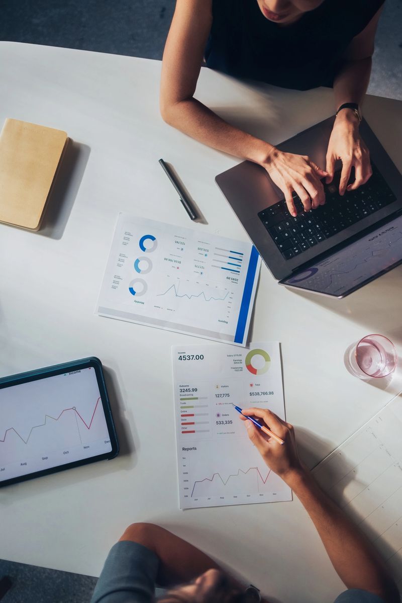 A collaborative team evaluates financial data using digital devices and printed reports, emphasizing teamwork and modern business methodologies in a workplace setting.