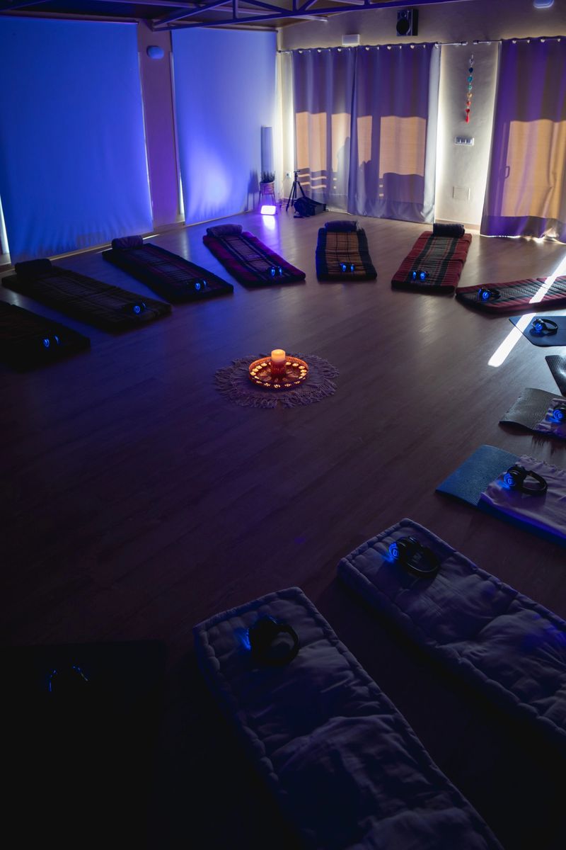 Yoga mats and earphones arranged in a circle around a candle in a dimly lit studio, ready for a breathwork session