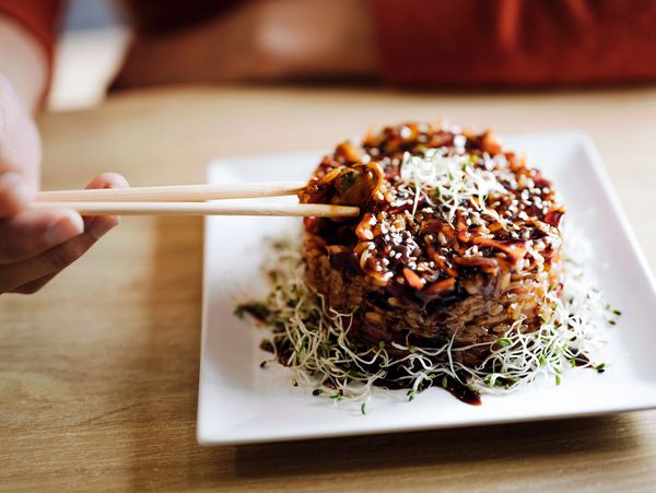 Person picking up a bite of rice dish with chopsticks from a white plate.